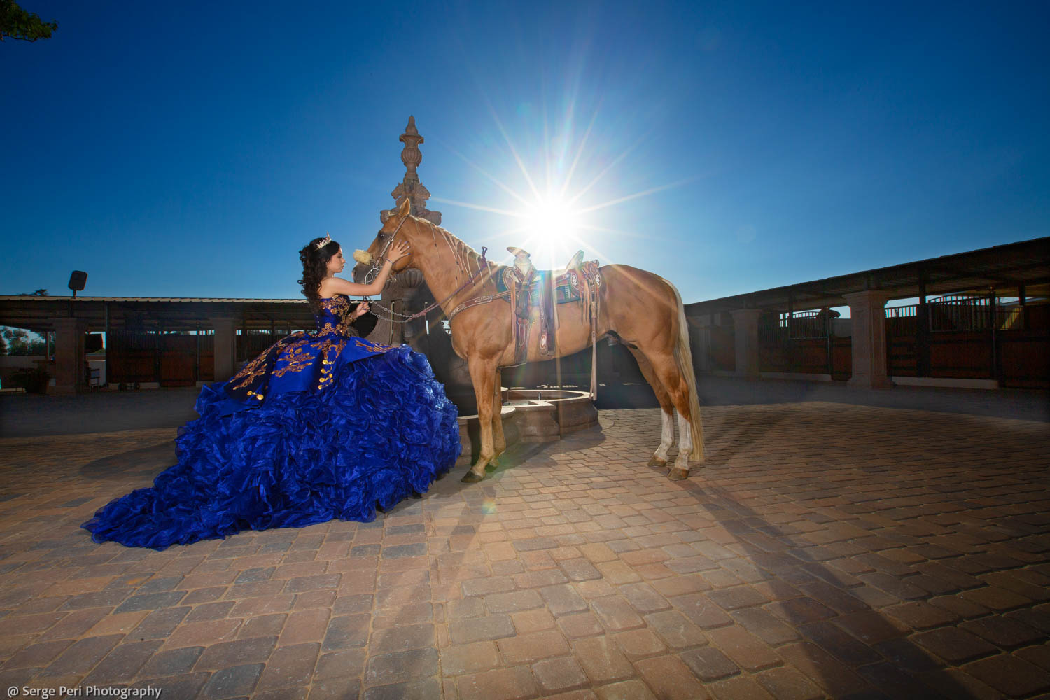 Quinceañera con vestido azul junto a un caballo al sol