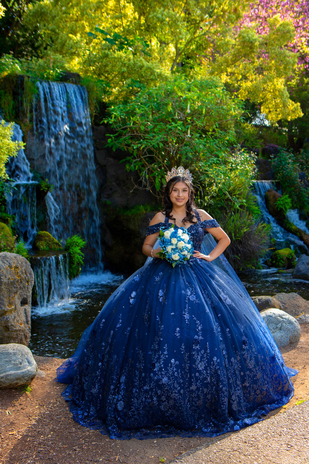 Quinceañera con vestido azul frente a una cascada